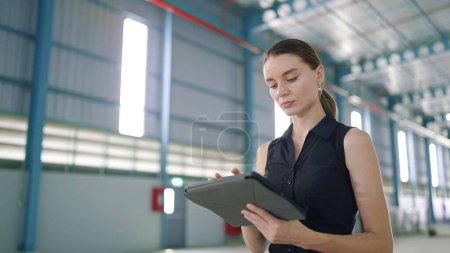 Téléchargez les photos : Gestionnaire femme caucasienne utilisant la tablette pour le travail et revérifier l'ordre ou le stock de produit dans l'usine ou l'entrepôt - en image libre de droit