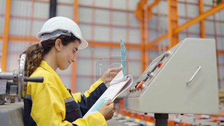 Photo for Young Hispanic latina women technician worker in uniform and helmet holding clipboard checking manufacturing control machine at industry factory - Royalty Free Image