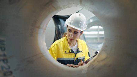 Photo for Hispanic latina woman engineer holding clipboard seen through a large pipe steel metal checking quality metal at industry - Royalty Free Image