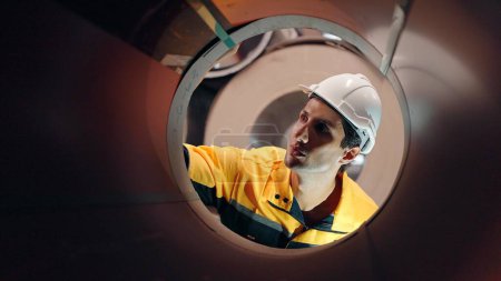 Téléchargez les photos : Ouvrier industriel hispanique latina homme en uniforme et casque de vérification de la qualité à l'intérieur de gros tuyaux en acier métal à l'usine de fabrication de l'industrie - en image libre de droit