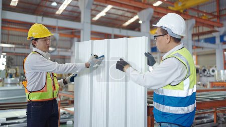 Téléchargez les photos : Deux travailleurs asiatiques professionnels en tenue uniforme de sécurité et contrôle de la qualité du toit en tôle à l'usine de fabrication de métal - en image libre de droit