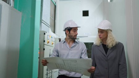 Téléchargez les photos : Deux ingénieurs de l'industrie dans les casques de construction à la recherche de plans de projet tout en marchant dans l'entrepôt - en image libre de droit