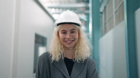 Téléchargez les photos : Portrait souriant de la belle ingénieur industriel femme en blanc stand de casque dur avec confiant et regardant caméra - en image libre de droit