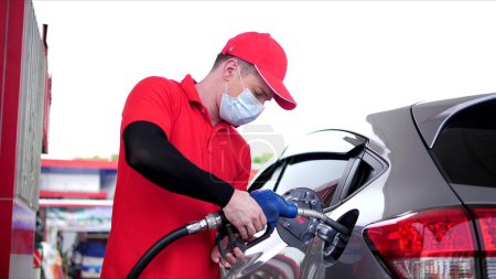 Téléchargez les photos : Travailleur asiatique employé en uniforme de travail ravitaillement à la voiture avec de l'essence tenant buse de remplissage à la pompe de la station-service - en image libre de droit