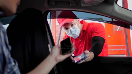 Téléchargez les photos : Client assis dans la voiture et payant la facture de gaz en scannant le code QR à la station-service, portant un masque facial à la station-service - en image libre de droit
