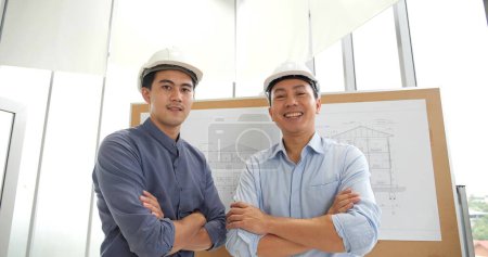 Foto de Dos arquitectos asiáticos profesionales de pie con los brazos cruzados y sonriendo mirando a la cámara - Imagen libre de derechos