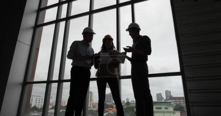 Photo for Silhouette of Asian group Architect and engineer construction workers on plans with a blueprint while working for teamwork. Architects discussing business plans - Royalty Free Image