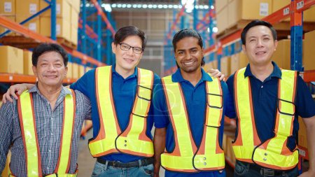 Téléchargez les photos : Portrait groupe de travailleurs d'entrepôt debout dans un grand centre de distribution d'entrepôt avec les bras croisés. En arrière-plan étagères avec des marchandises. Travailleur souriant et regardant la caméra - en image libre de droit