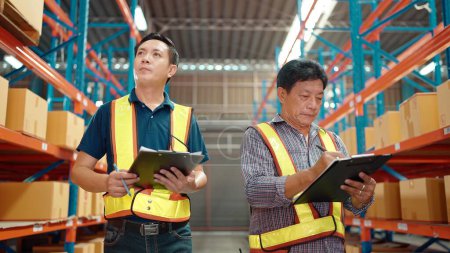 Téléchargez les photos : Deux travailleurs asiatiques avec liste vérifiant l'état des stocks dans l'entrepôt de l'industrie de l'usine d'affaires. Concept d'industrie logistique - en image libre de droit