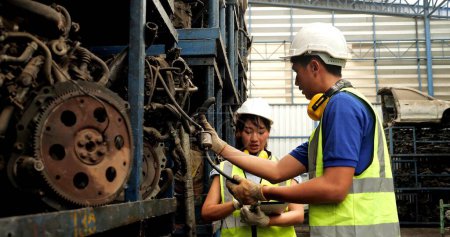 Foto de Dos trabajadores asiáticos técnicos con traje de seguridad de verificación de casco de stock de piezas de automóviles usados por tableta digital en la fábrica industrial - Imagen libre de derechos