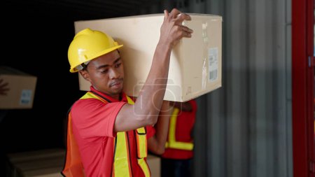 Photo for Young African American black workers courier lifting cargo boxes stacking on pallet in warehouse wearing engineer suit and helmet for safety. Shipment boxes. Warehousing storage - Royalty Free Image