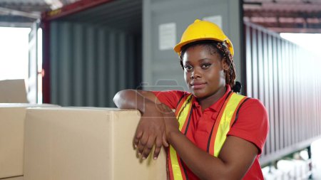 Photo for Young African American black woman worker looking at camera wearing engineer suit and helmet for safety. in warehouse, International export business concept - Royalty Free Image