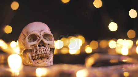 Téléchargez les photos : Crâne humain en plastique sur un noir d'horreur avec un fond bokeh clair. Halloween de vacances, toile de fond du thème d'Halloween. espace de copie - en image libre de droit
