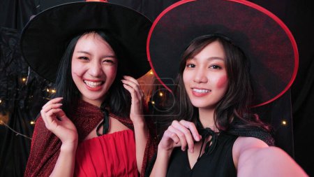 Foto de Feliz dos mujeres asiáticas en disfraces de Halloween sonriendo y tomando selfie en la fiesta de la casa, amigos divertidos en disfraces en la fiesta de Halloween de la noche - Imagen libre de derechos