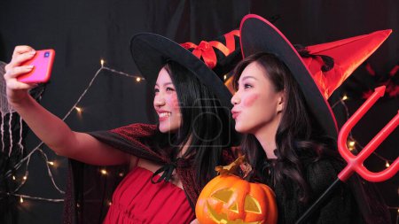 Foto de Dos mujeres asiáticas en disfraces de Halloween sonriendo y tomando selfie en casa fiesta de noche - Imagen libre de derechos