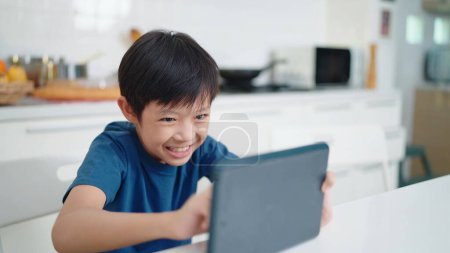 Foto de Niño asiático jugar juegos en la tableta en casa los fines de semana. Los niños adictos al concepto de juegos - Imagen libre de derechos