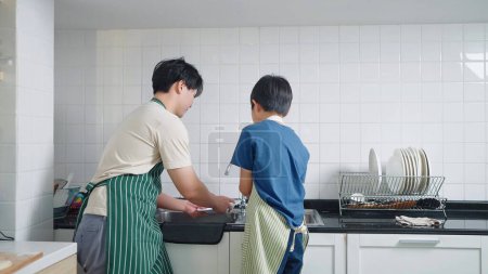 Foto de Vista posterior de padre asiático enseñando a su hijo a lavar los platos en la cocina en casa. Concepto de padre único - Imagen libre de derechos