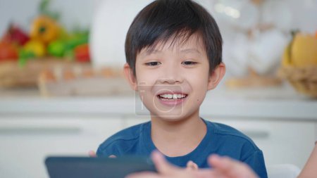 Foto de De cerca sonriente cara de chico asiático viendo dibujos animados en línea en la tableta en vacaciones en casa - Imagen libre de derechos