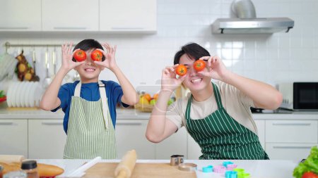 Photo for Asian father and cute little son in apron having fun with tomato at kitchen room. Cooking and family times concept. Single father concept - Royalty Free Image