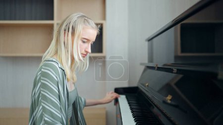 Foto de Adolescente con cabello rubio estudiando para tocar el piano en casa. Educación, concepto de habilidades - Imagen libre de derechos