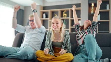 Photo for Cheerful happy Caucasian family cheering for favorite team and it scoring goal and winning game. mother, father and daughter watching TV with sports celebration cheers, hands holding up - Royalty Free Image