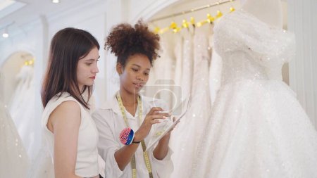 Photo for Two professional women fashion designer using tablet for design white wedding dress at wedding studio - Royalty Free Image