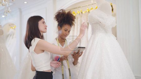 Photo for Two professional women fashion designer discussing and design white wedding dress at wedding studio - Royalty Free Image
