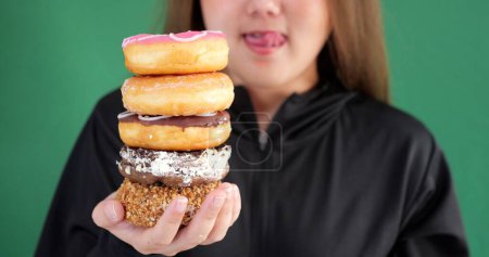 Foto de Primer plano de la mujer posando aislado sobre fondo verde elegir entre donuts dulzuras - Imagen libre de derechos