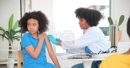 Téléchargez les photos : Des enfants afro-américains se font vacciner à la clinique ou à l'hôpital, avec une infirmière s'injectant le vaccin pour obtenir une immunité pour se protéger. vaccin pour enfants concept - en image libre de droit