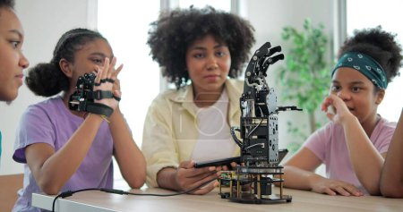 Foto de Grupo de estudiantes afroamericanos adolescentes que aprenden sobre la escuela de brazos robóticos, profesor que asiste a estudiantes de primaria en el aula de ingeniería robótica. Concepto de tecnología e innovación - Imagen libre de derechos