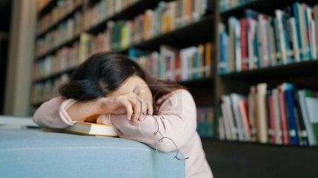 Foto de Cansada estudiante asiática con gafas durmiendo en los libros de la biblioteca - Imagen libre de derechos