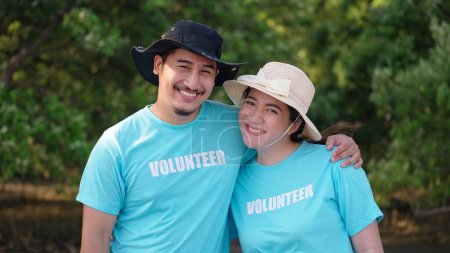 Couple asiatique en t-shirts volontaires souriant regarder les aides-caméras planter des arbres dans les forêts de mangroves pour la protection de l'environnement et l'écologie, réduire le réchauffement climatique
