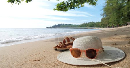 Téléchargez les photos : Plage d'été avec chapeau de paille, lunettes de soleil et tongs sur fond de plage de sable - en image libre de droit