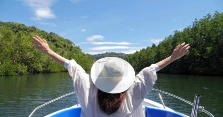 Foto de Vista posterior de las mujeres turísticas disfrutando de la naturaleza en el barco levantando las manos respirar aire fresco en el agua a través del bosque de manglares a lo largo. Viaje cóncavo - Imagen libre de derechos