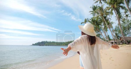 Foto de Vista posterior de la mujer de pie en la playa y levantando las manos. vacaciones, vacaciones, relajarse en el estilo de vida de verano - Imagen libre de derechos