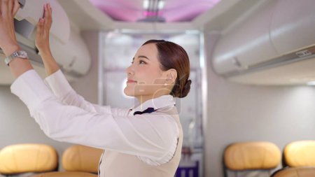 Téléchargez les photos : Hôtesse asiatique en uniforme hôtesse de l'air enregistrement et fermeture du compartiment à bagages de l'avion avant le décollage - en image libre de droit