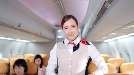 Photo for Attractive young Asian stewardess in uniform looking and smiling to the camera in airplane, Cabin crew or air hostess occupation concept - Royalty Free Image
