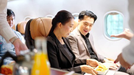 Foto de Asistente de vuelo que sirve bebidas y habla con los pasajeros en el avión. Servicio de línea aérea - Imagen libre de derechos