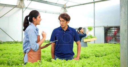 Foto de Agricultor asiático mujer celebración tableta hablando con el cliente asiático hombre de verduras orgánicas de la granja de exportación al mercado - Imagen libre de derechos