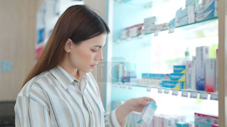 Téléchargez les photos : Belle jeune femme asiatique debout entre les étagères à la recherche et le shopping pour les produits de suppléments de médecine à la pharmacie - en image libre de droit