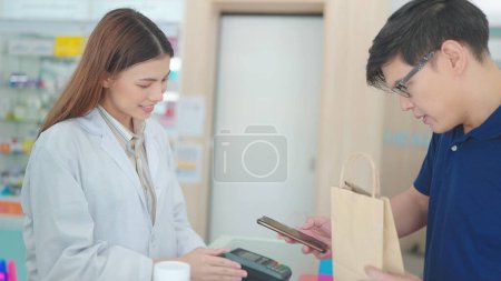 Foto de Los clientes masculinos asiáticos compran medicamentos con farmacéuticos en farmacias y escanean códigos de barras para pagos - Imagen libre de derechos