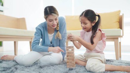 Photo for Asian mother and daughter playing jenga on the floor. Happy little daughter play toy wooden block with mother spending time together on holiday in living room at home - Royalty Free Image