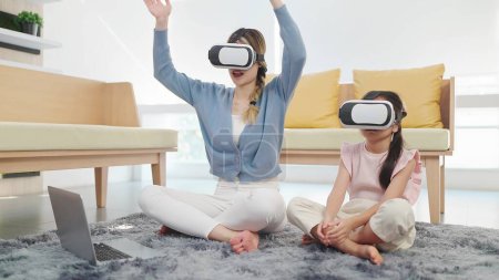 Photo for Asian mother and daughter wearing glasses of technology virtual reality headset playing game on labtop sitting on floor in living room - Royalty Free Image