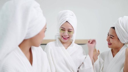 Photo for Group of beautiful young asian women in bathrobe and towels on heads with collagen patch on under eyes and enjoy talking together. Woman with under eye collagen pads - Royalty Free Image