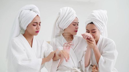 Téléchargez les photos : Groupe de jeune belle femme asiatique en peignoir blanc profiter applique crème hydratante à la peau sentant odeur parfumée. Concepts de soins de la peau - en image libre de droit