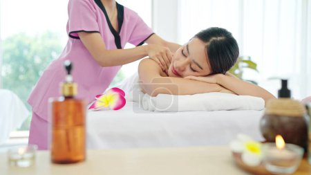 Téléchargez les photos : Femme asiatique saine et belle en serviette blanche couchée sur un lit de spa yeux fermés relaxant recevant un massage du cou et des épaules. Concept de traitement Spa - en image libre de droit