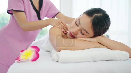Foto de Mujer asiática joven feliz y relajada tumbada en la cama de masaje con los ojos cerrados y relajada mientras masajea la espalda y los hombros. Concepto de relajación corporal - Imagen libre de derechos
