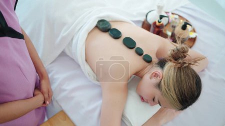 Photo for Relaxed woman in white towel lying on massage bed closed eyes having hot stones on back. Wellness and body relaxation therapy - Royalty Free Image