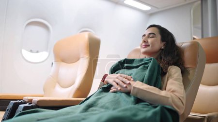 Foto de Joven pasajera latina hispana durmiendo en el asiento con manta mientras viaja en avión. La mujer viaja en vuelo largo - Imagen libre de derechos
