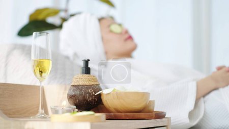Téléchargez les photos : Fermez l'équipement de spa avec une femme allongée sur un lit de spa se sentant détendue avec des tranches de concombre sur les yeux en arrière-plan bleu. Concept d'aromathérapie Spa - en image libre de droit